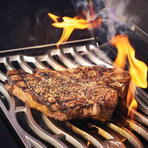 A juicy steak sizzles on a grill, surrounded by vibrant flames, showcasing a perfect cooking moment.